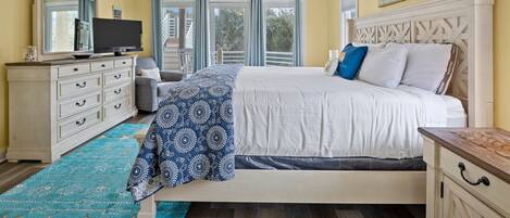 A bedroom with a bed, a television, a dresser, and a window with curtains.
