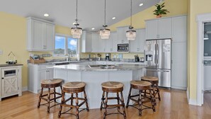 A kitchen with a large island, white cabinets, stainless steel appliances, and three wooden stools. - 3rd Row Oceanview,Private pool,hot tub,pet friendly,very short walk to beach (Emerald Isle)