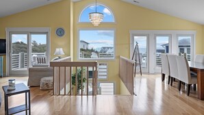 A spacious living area with a high ceiling, large windows, and a balcony with a view. - 3rd Row Oceanview,Private pool,hot tub,pet friendly,very short walk to beach (Emerald Isle)