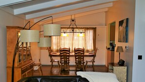 Un salon avec un canapé en cuir noir, un coin repas avec des chaises en bois et une table, et un coin cuisine avec un meuble et une lampe.