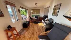 A cozy living room with a wooden floor, a grey sofa, a wooden coffee table, and a dining area with a table and chairs.