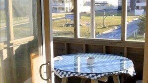Eine Holzterrasse mit Glastür, Deckenventilator, rundem Tisch mit kariertem Tischläufer und hölzernen Bänken.