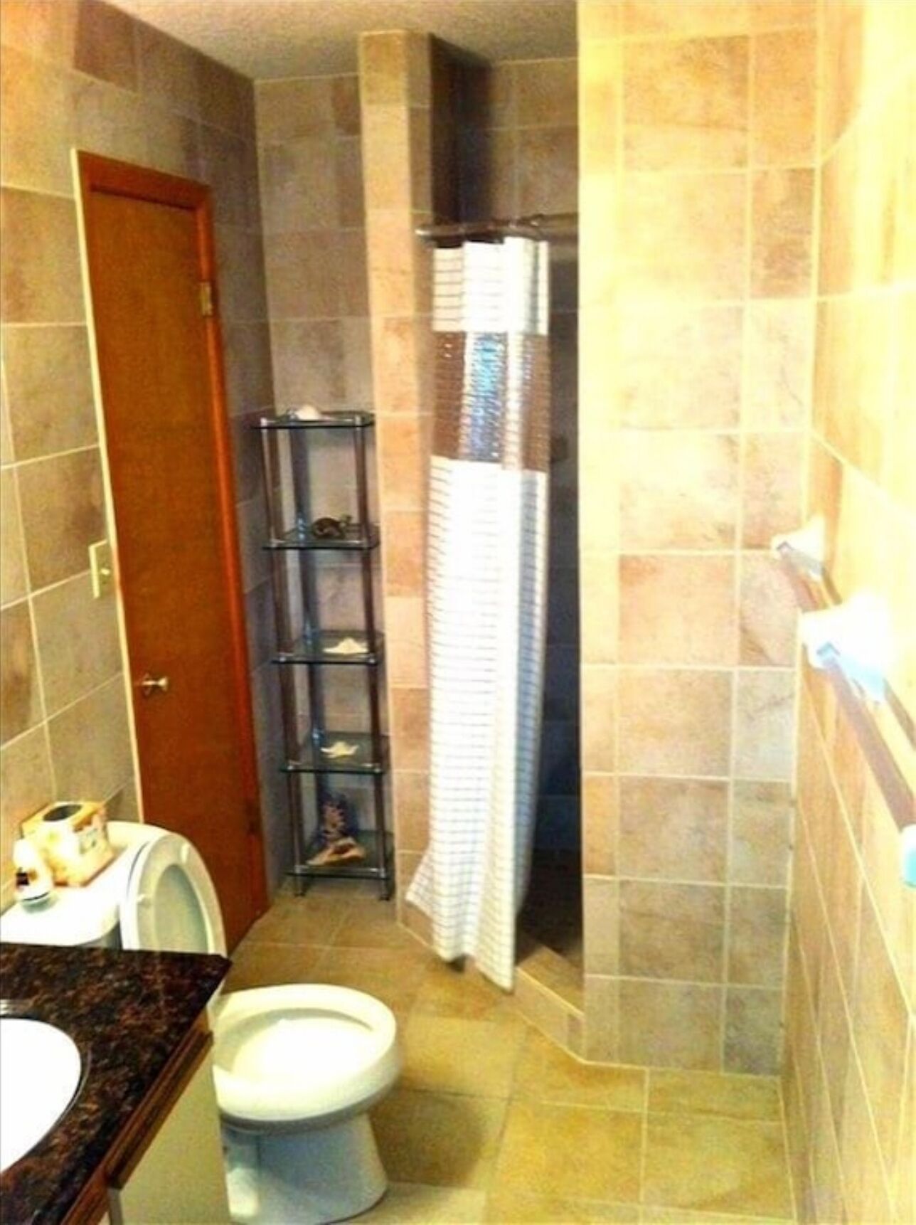 A bathroom with a toilet, a sink, a shower, and a shelf with toiletries.