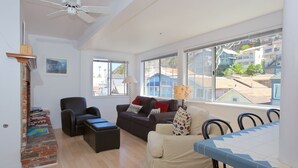 A spacious living room with a ceiling fan, a fireplace, and large windows offering a view of the neighborhood. - Spacious 5 bedroom home, 1 block from beach (Avalon)