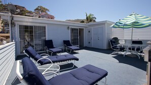 A covered outdoor patio with lounge chairs and a table, a sliding glass door, and a striped umbrella. - Spacious 5 bedroom home, 1 block from beach (Avalon)