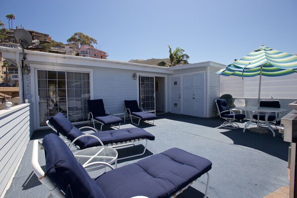 A covered outdoor patio with lounge chairs and a table, a sliding glass door, and a striped umbrella.