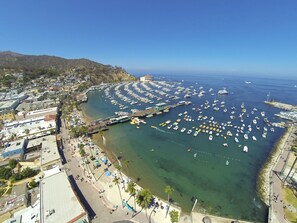 An aerial view of a coastal town with a marina filled with boats, a beach with umbrellas, and buildings along the waterfront.