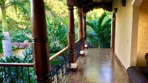 A covered balcony with tiled flooring, wooden columns, and a wrought iron railing.