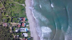 An aerial view of a coastal area with houses near the beach, a road, and a clear view of the ocean.