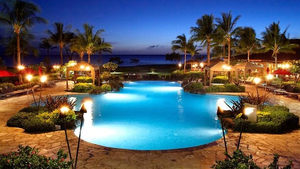 A nighttime swimming pool with palm trees and lounge chairs, surrounded by a stone deck and a view of the ocean. - ❤️Luxury 2 BD Condo at Honua Kai Resort on the Beach ❤️ (Kaanapali)