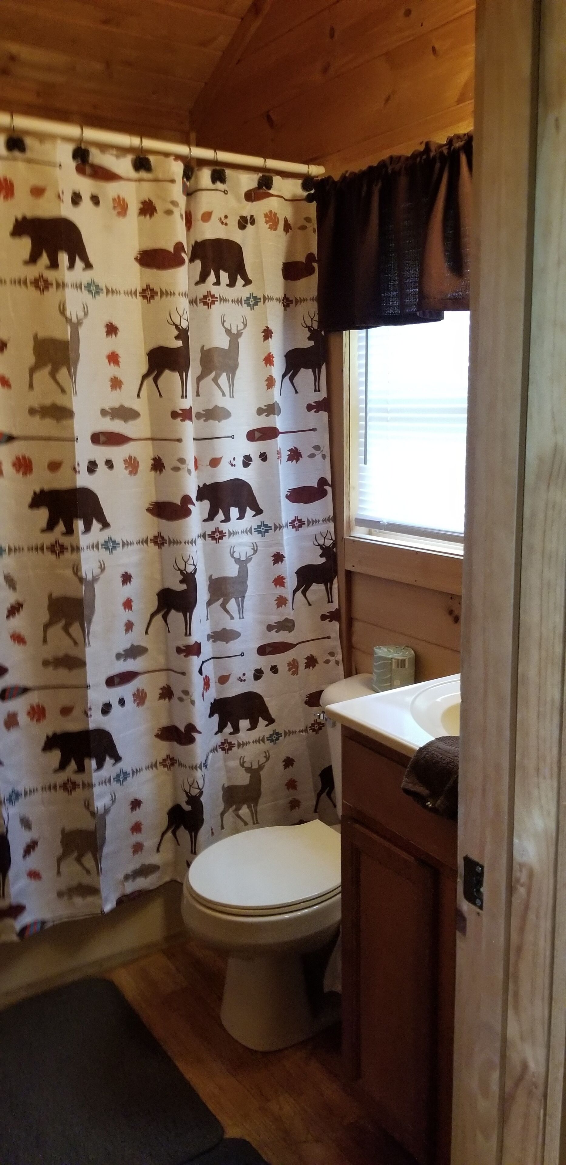 A small, rustic bathroom with a toilet, a sink, and a shower curtain featuring animal prints.