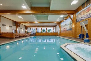 An indoor swimming pool with wooden beams, a hot tub, and a mural on the wall.