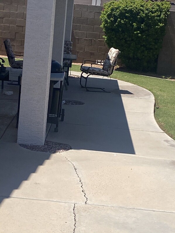 An outdoor patio area with a concrete floor, a table, chairs, and a covered seating area.