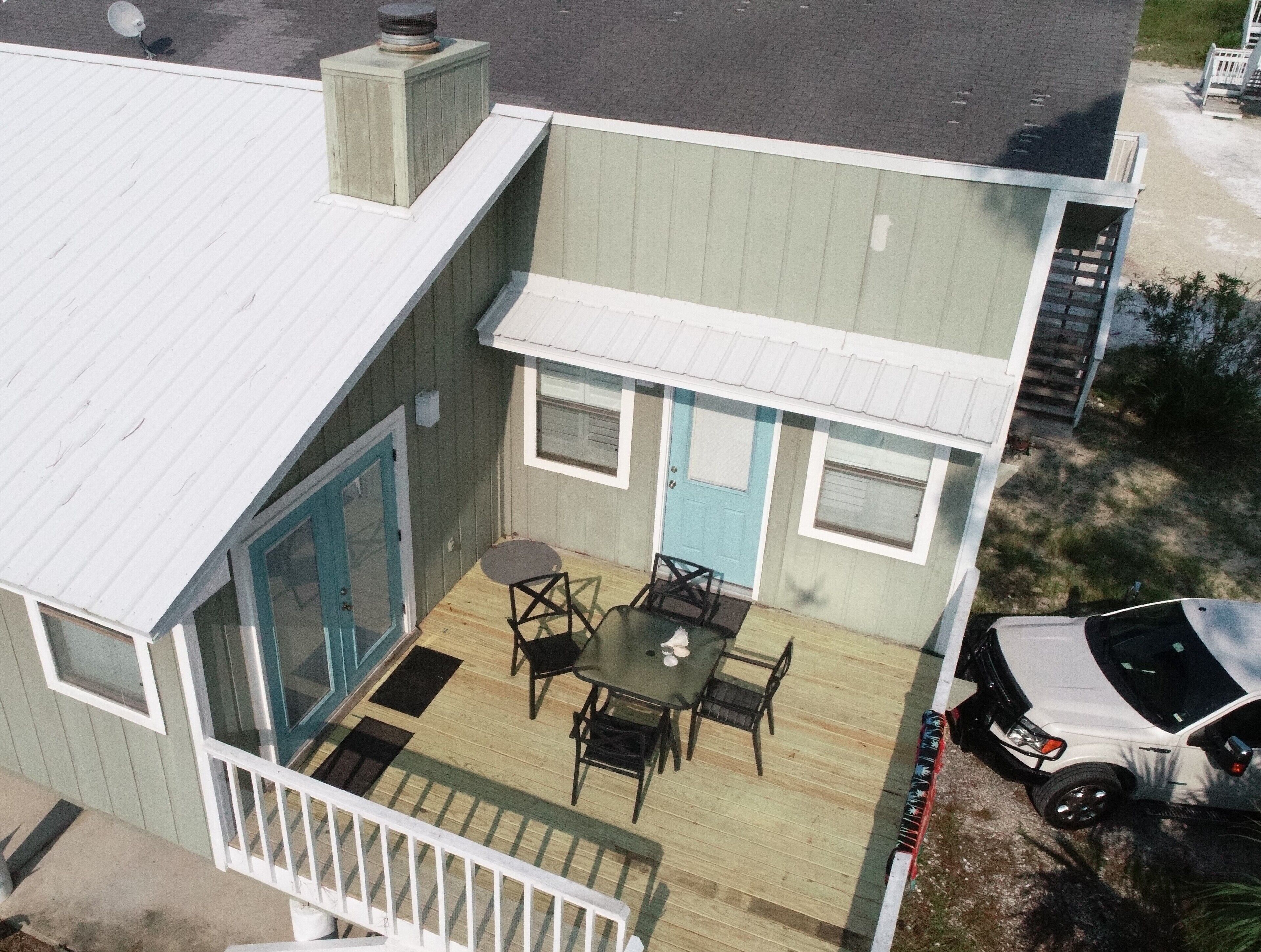 A two-story house with a balcony, a dining area with a table and chairs, and a garage with a car parked inside.