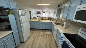 Een keuken met lichtblauwe kastjes, een witte koelkast, een magnetron en een fornuis. Er is een houten aanrecht en een vloerkleed op de vloer.