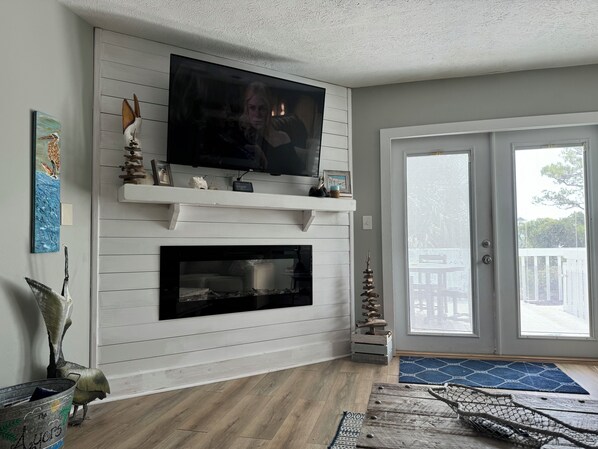 A living room with a fireplace, a mounted TV, and a door leading outside.