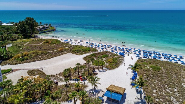 A beach with clear blue water, white sand, and numerous blue umbrellas. - Siesta Key private beach access (Sarasota)