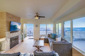 A spacious living room with a large TV, a fireplace, and a view of the ocean.