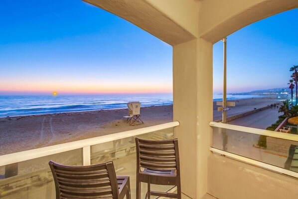 A balcony with two chairs overlooking a beach at sunset.