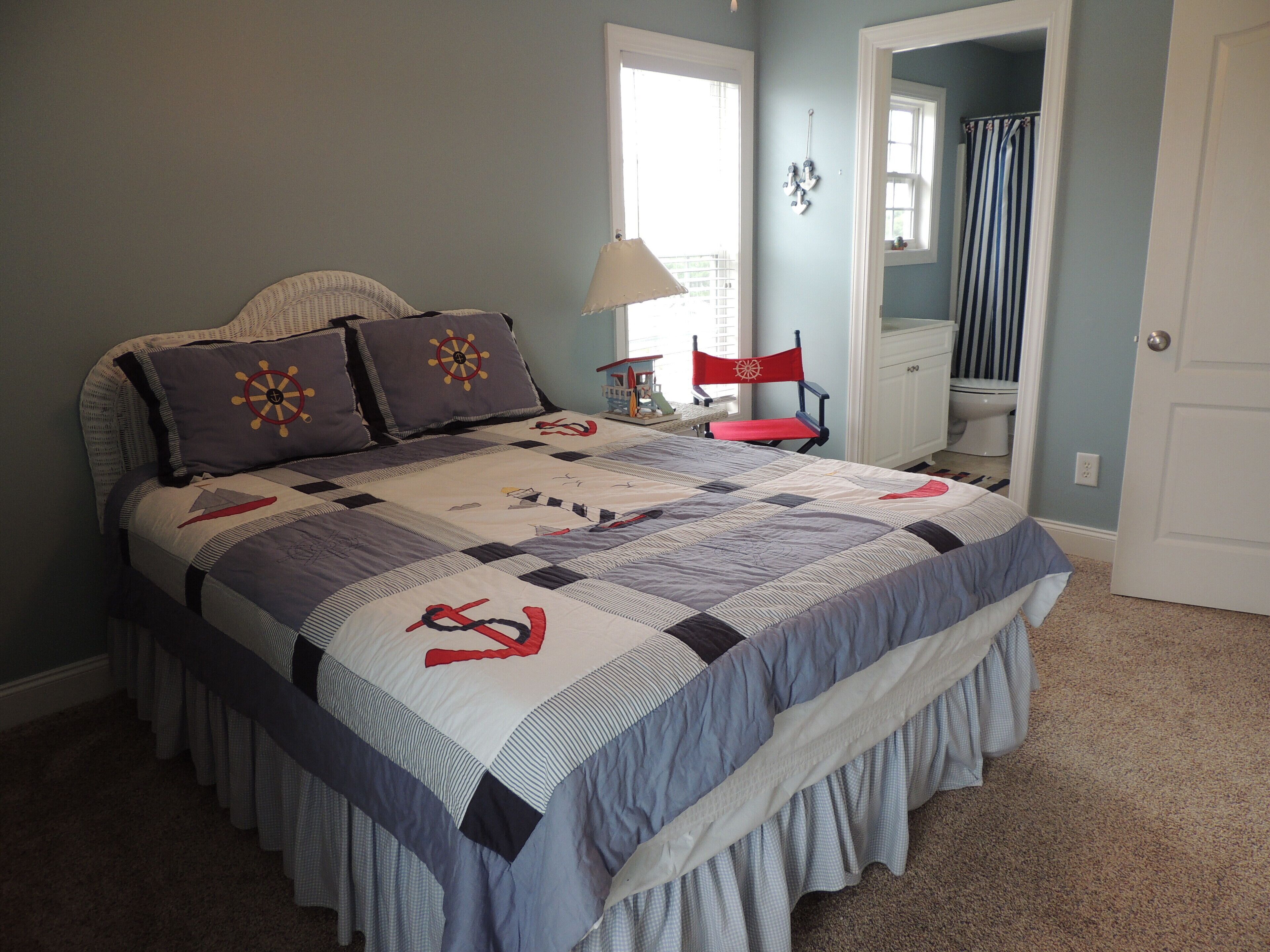 A bedroom with a bed, a chair, a lamp, and a view of the bathroom.