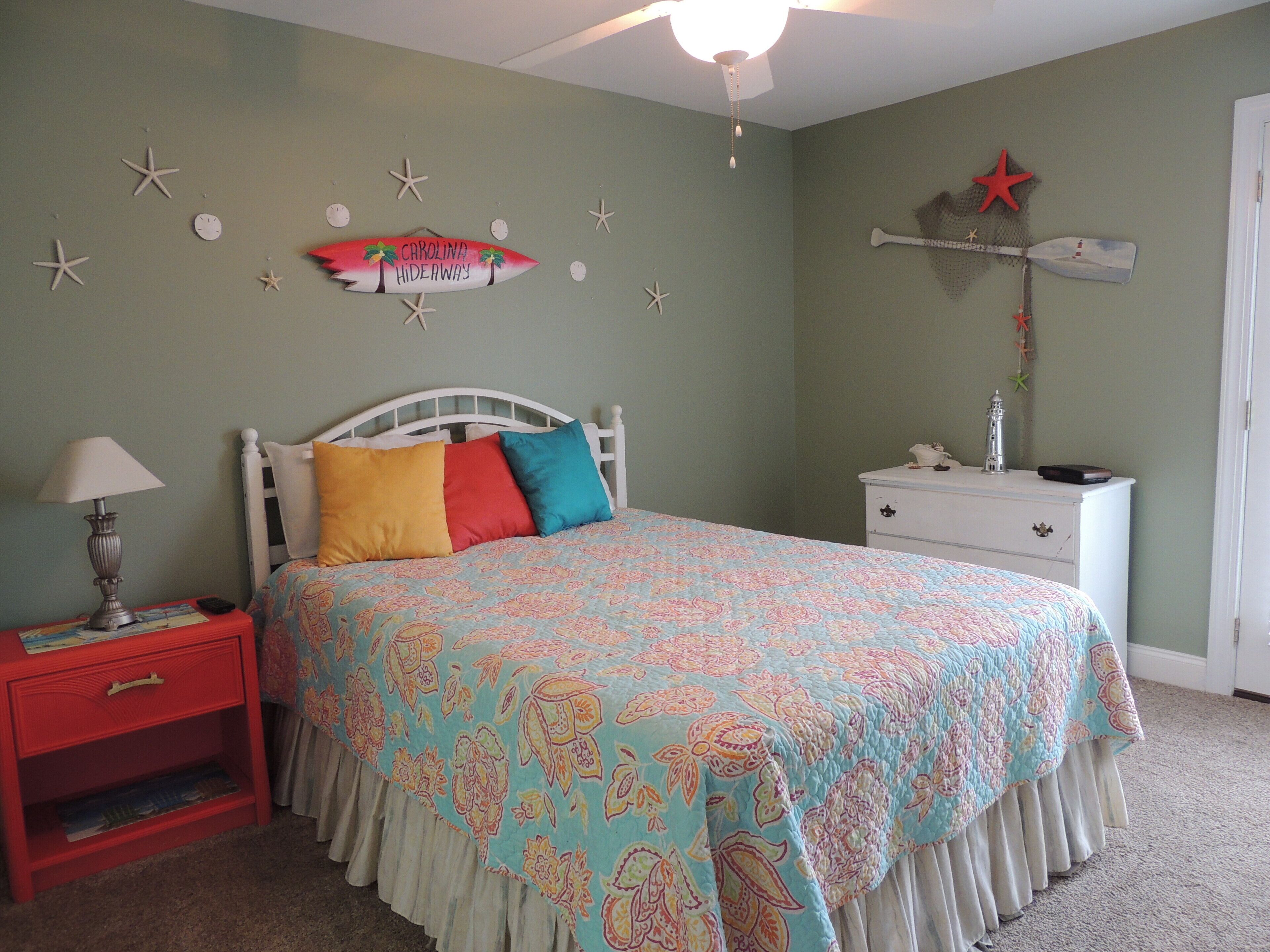 Un dormitorio con cama, mesita de noche, cómoda y decoración de estrellas de mar y una tabla de surf en la pared.