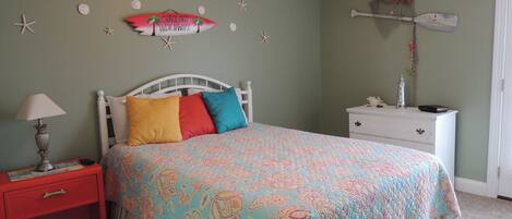 Un dormitorio con cama, mesita de noche, cómoda y decoración de estrellas de mar y una tabla de surf en la pared.