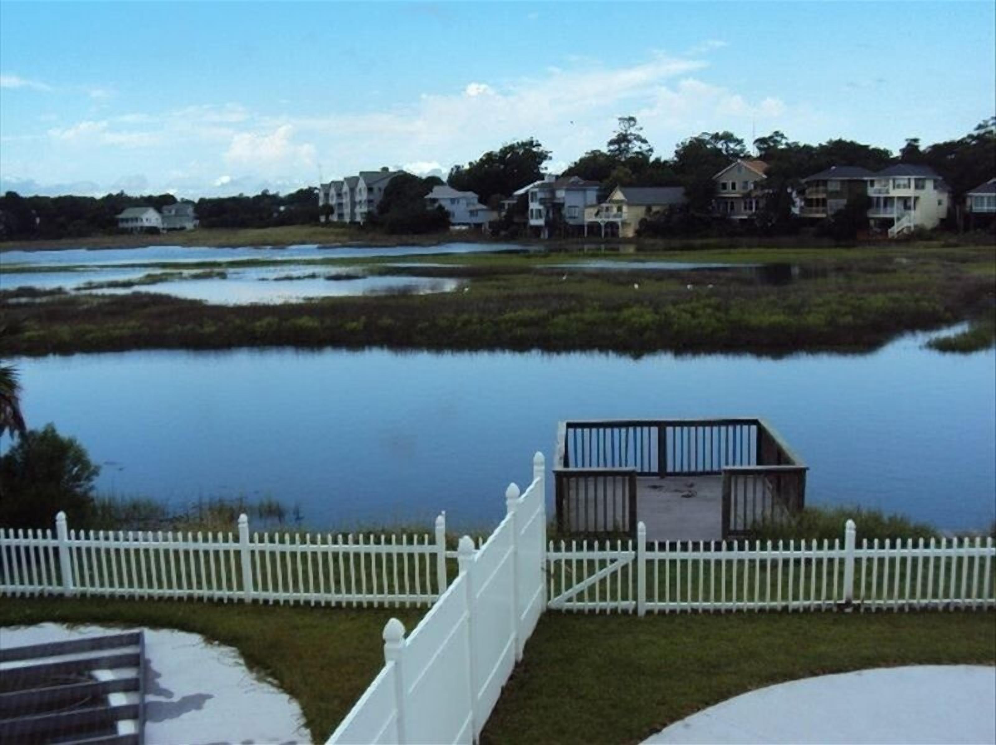 A waterfront property with a dock, white picket fence, and houses in the background.