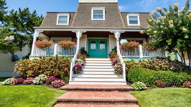 Une maison à deux étages avec une porte verte, un porche blanc et un petit balcon.