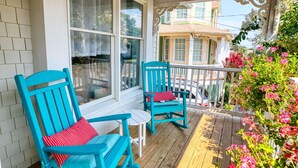 Une véranda avec des chaises turquoise et une petite table, une terrasse en bois et une vue sur une maison dotée d’une véranda.