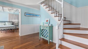 Une pièce avec un plancher en bois, un lit doté d’une tête de lit blanche, un escalier avec des rampes blanches et un mur orné d’un tableau encadré.