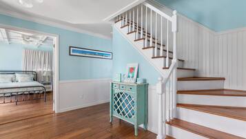 A room with a wooden floor, a bed with a white headboard, a staircase with white railings, and a wall with a framed picture.