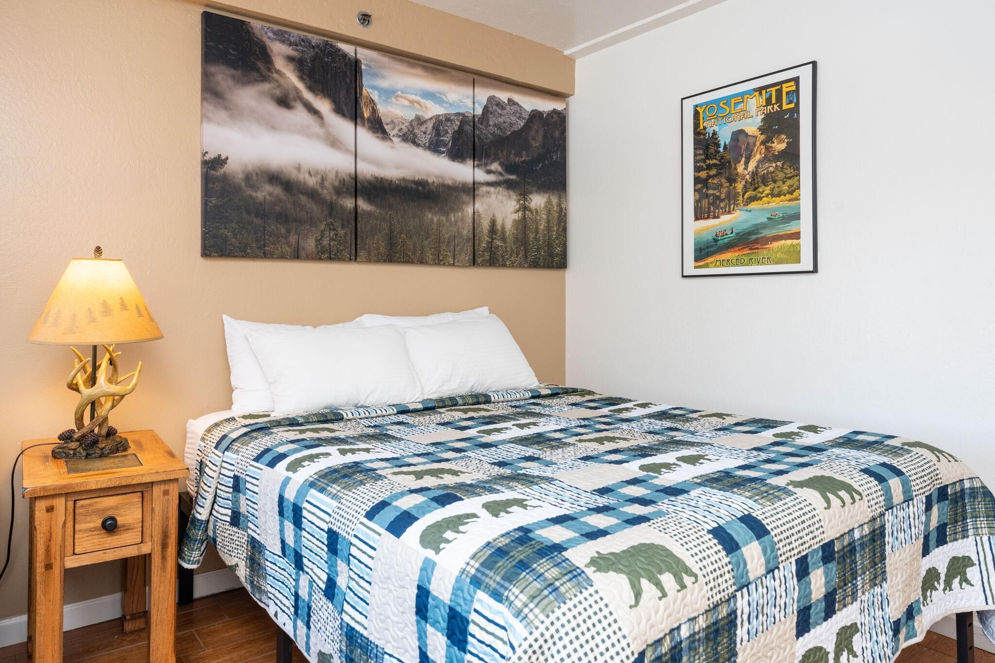 Une chambre à coucher avec un lit, une table de chevet avec une lampe, un tableau accroché au mur représentant le parc national de Yosemite, et une affiche encadrée de Yosemite.