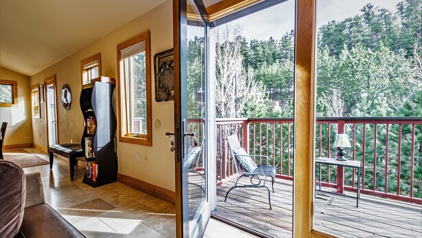 Une pièce dotée d’une grande porte-fenêtre coulissante qui donne sur un balcon avec une balustrade rouge et une vue sur les arbres.