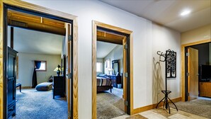Un couloir avec des portes en bois donnant sur une chambre et un salon. On peut apercevoir un trépied près de la porte de droite.