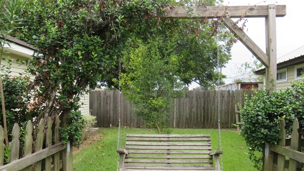 Ein hölzernes Schaukelgestell in einem Garten mit Holzzaun und einer überdachten Holzpergola.