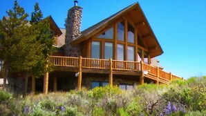 A large log cabin with a stone chimney, wooden deck, and large windows. - Exclusive Family Luxury Mountaintop Lodge on 43 acres (Granby)