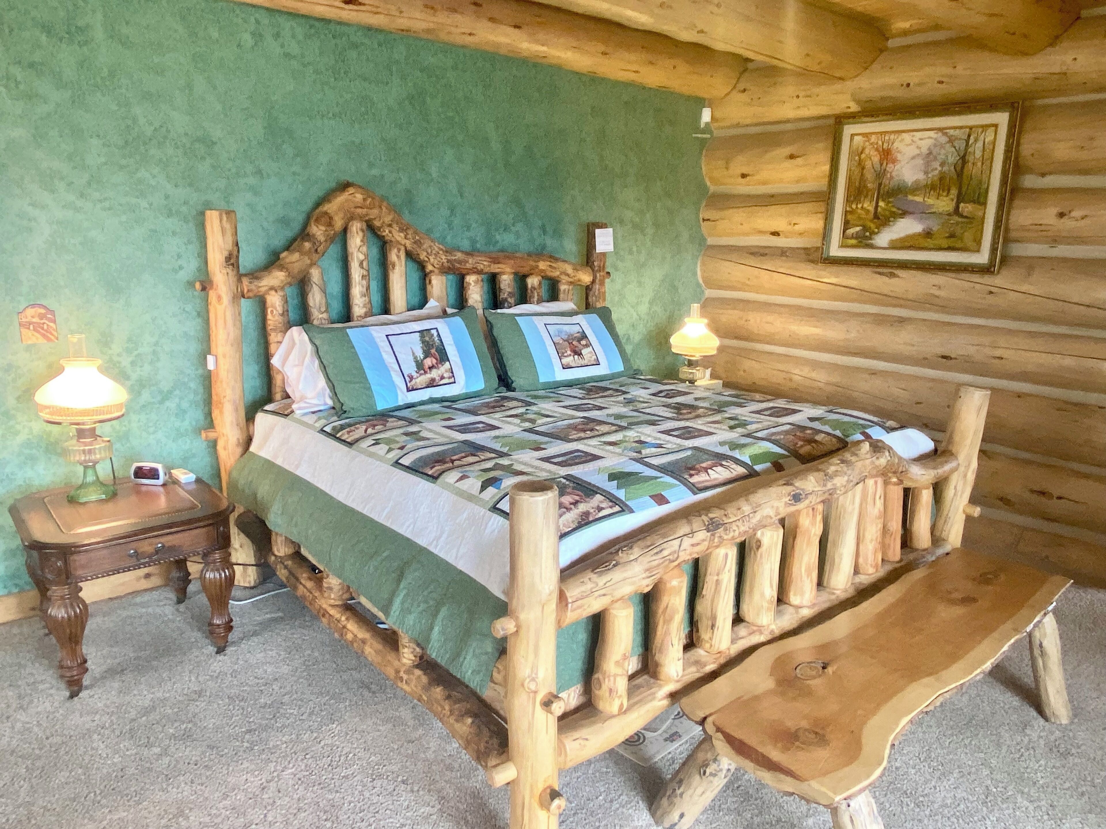 Una cama de madera rústica con colcha, una mesita de noche con lámpara y un banco.