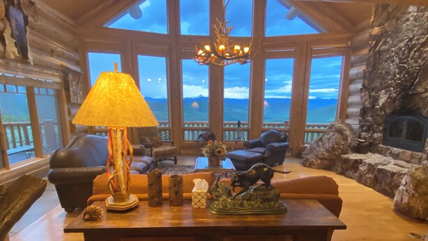 A cozy living room with a large window, a fireplace, and a wooden table with decorative items. - Exclusive Family Luxury Mountaintop Lodge on 43 acres (Granby)