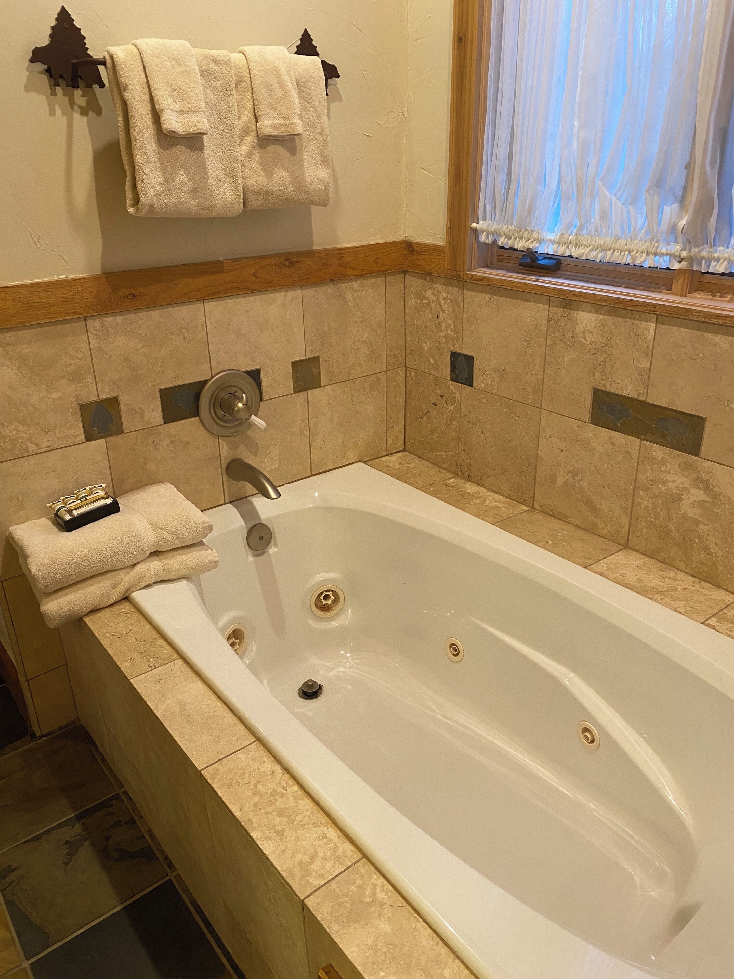 Une salle de bain avec une grande baignoire, un porte-serviettes avec une serviette, et une fenêtre avec des rideaux légers.