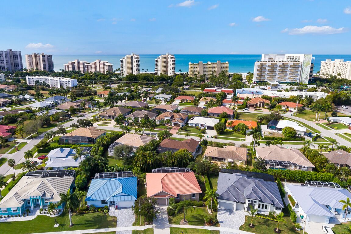 Zona residencial costera con diversos estilos de casas, un puerto deportivo y edificios altos al fondo.