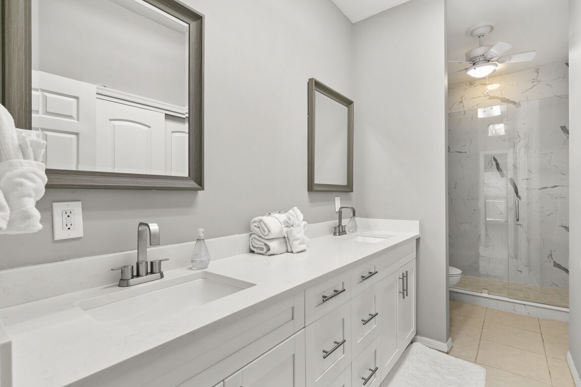 A modern bathroom with a large mirror, two sinks, a shower, and a walk-in shower.
