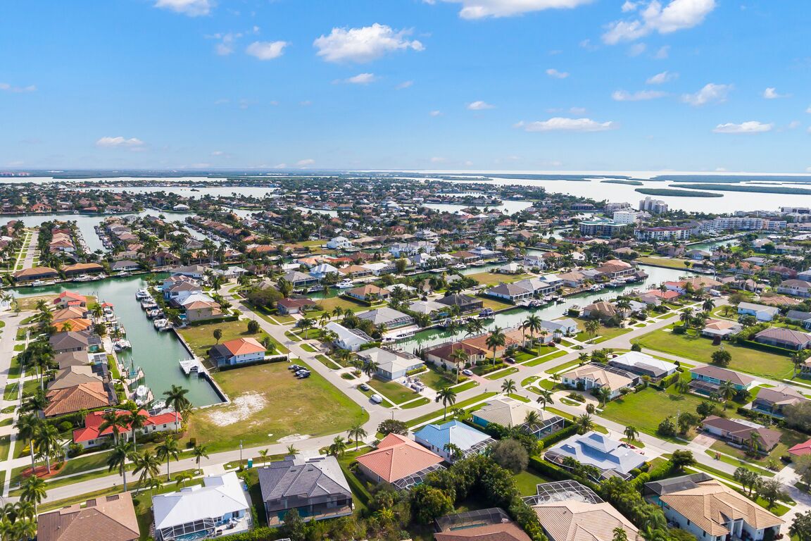 An aerial view of a residential area with houses, a marina, and a large body of water in the background.