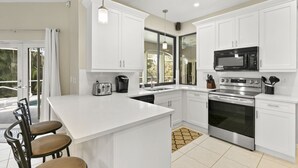 Une cuisine moderne avec des meubles blancs, une cuisinière en acier inoxydable, un four à micro-ondes et un grand îlot central doté de tabourets de bar.