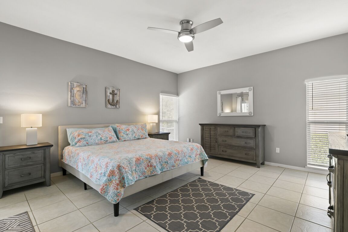 A bedroom with a bed, nightstands, a dresser, a ceiling fan, and artwork on the walls.