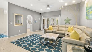 Un salon moderne avec un canapé d’angle beige, une table basse en verre et un tapis à motifs bleus.