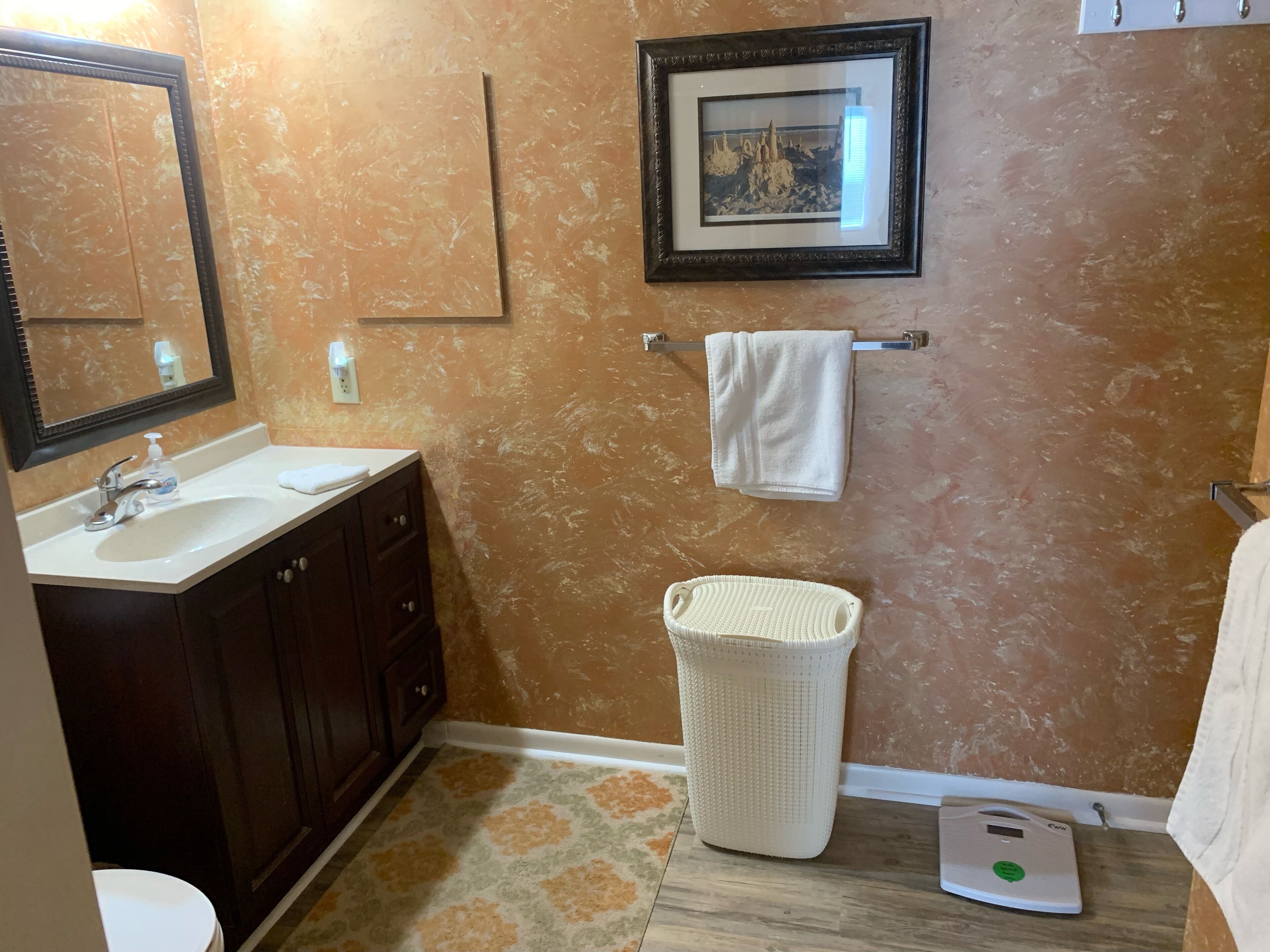 Une salle de bain équipée d’un lavabo, d’un miroir, d’un porte-serviettes et d’une balance.