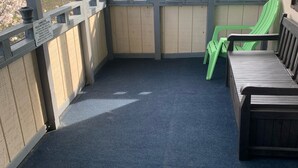 Un balcón cubierto con una alfombra azul, un banco de madera y una silla verde.