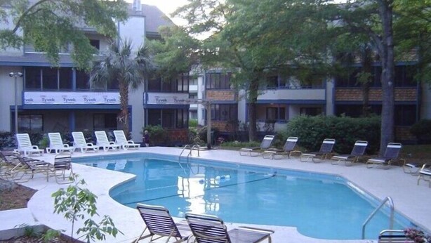 Una piscina con sillas de descanso y un edificio con señalización 'Tyvek' al fondo.