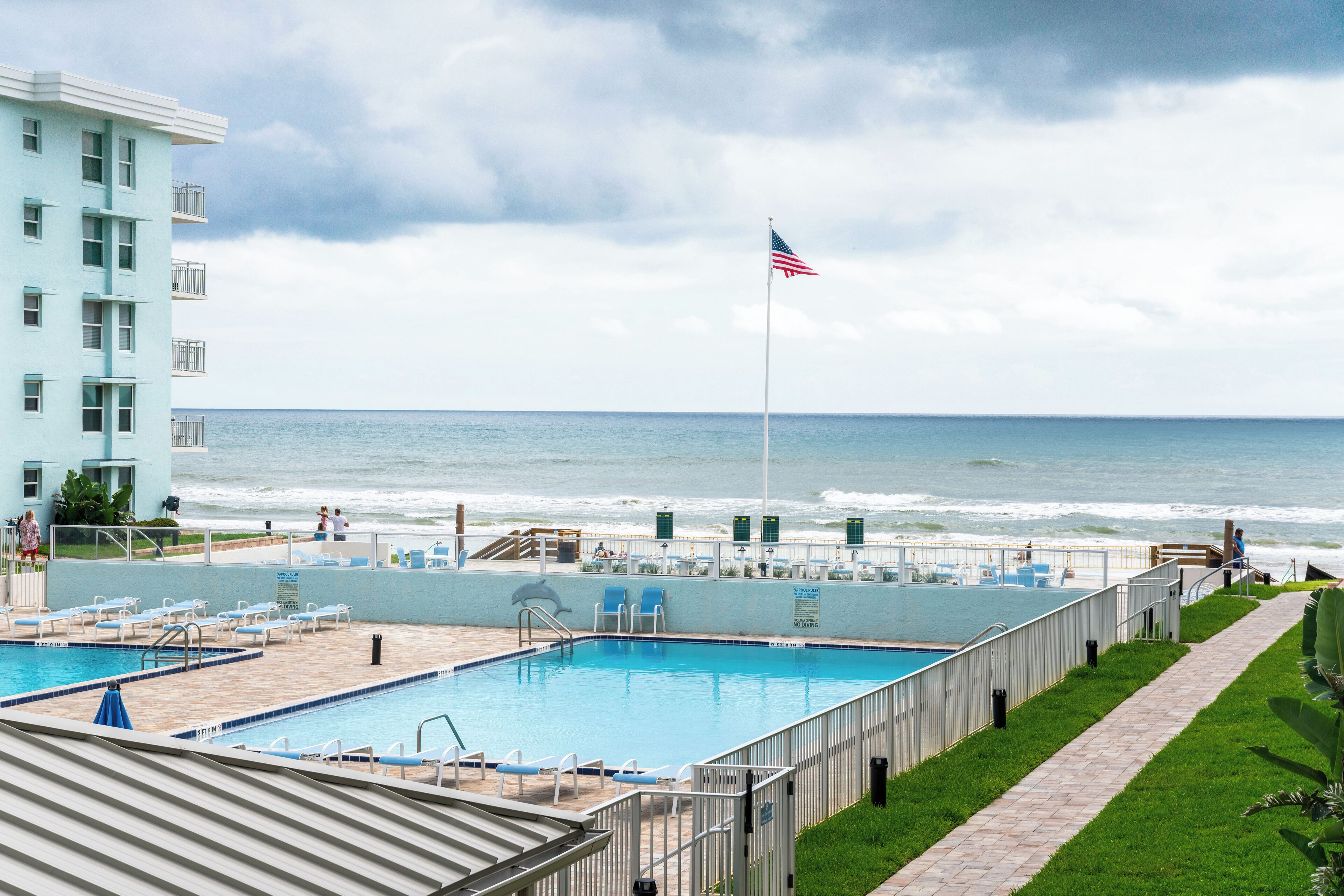 Une piscine avec vue sur l’océan, un drapeau et un bâtiment doté de balcons.