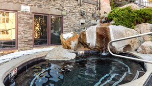 Un bain à remous doté d’une cascade, entouré de rochers et bordé d’un mur de pierres.